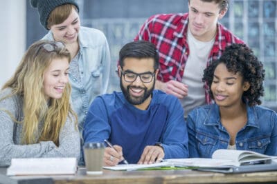 A group of young adults are in their university classroom. They are gathered around a table to study together.