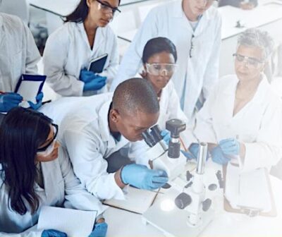 A group of scientists work in a lab with microscopes. Text on the image reads: 