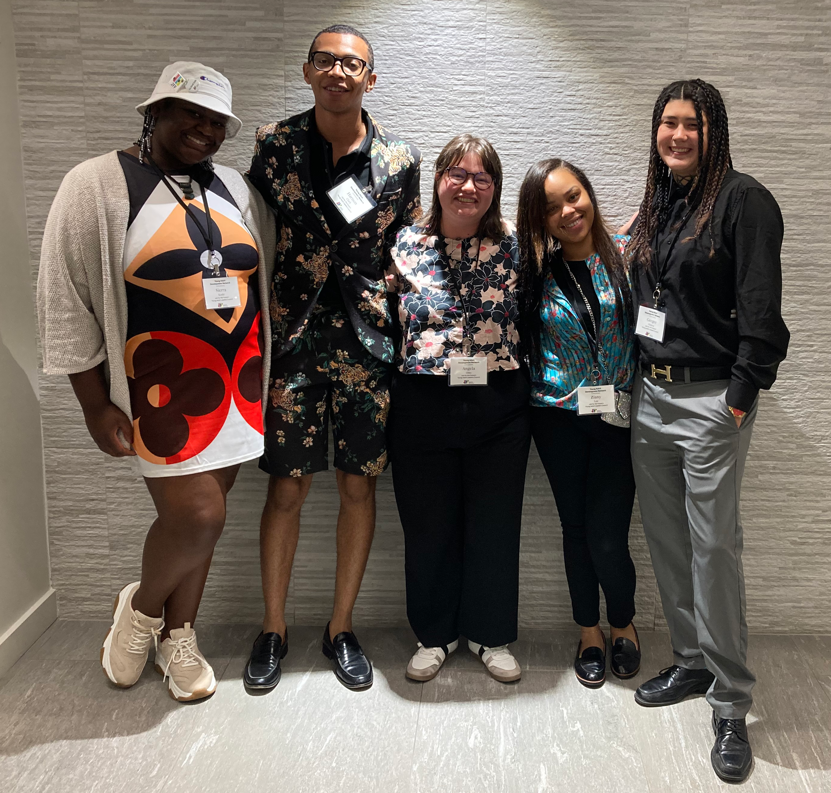 Five people standing together in a hallway, smiling and wearing conference name tags.