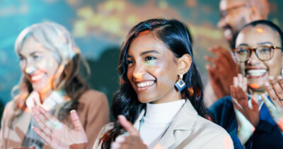 A group of people smiling and clapping, with colorful lights projected on them.